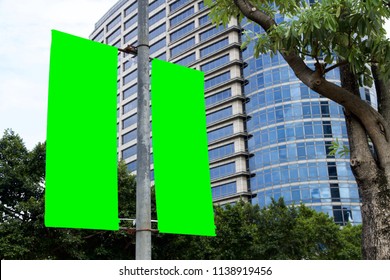 The Blank Advertising Banner Suspended On The Street Lamp Pole With The Tree And Building Facade Background.