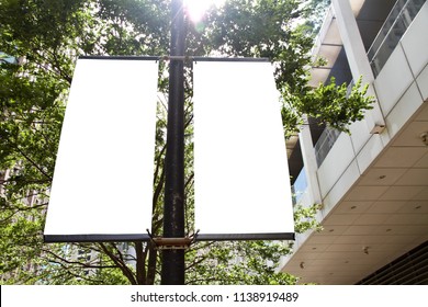 The Blank Advertising Banner Suspended On The Street Lamp Pole With The Sunlight From The Tree Background.