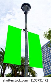 The Blank Advertising Banner Suspended On The Street Lamp Pole With The Tree And Building Facade Background.