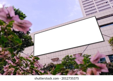 Blank Advertising Poster Banner Mockup On Building Exterior, Flowers Plants In Foreground; Large Digital Lightbox Display Screen. Billboard Poster, Out-of-home OOH Media Display Space