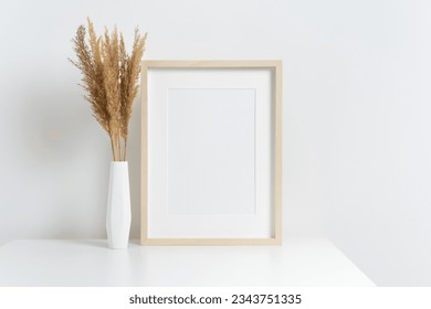 Blank artwork frame mockup with stylish dry grass decoration in white vase, scandinavian room interior