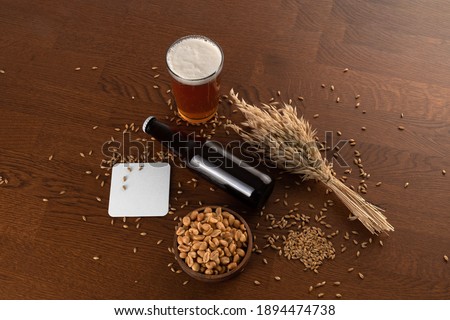Blank beer bottle and glass with beer, peanuts bowl, wheat, malts, beer pad, on a wooden background, craft beer mockup templates, with empty space to place your label or design