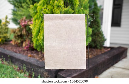 Blank beige garden flag in front of bushes, mock up
