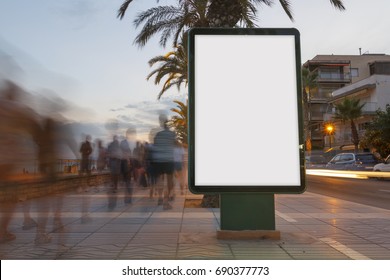Blank billboard in a footpath at sunset, with blurred people walking