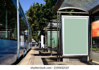 blank billboard lightbox ad panel at busstop. bus shelter with poster sign advertising. mockup base. communication placeholder. blue tram detail on the side. streetcar stop. city park background