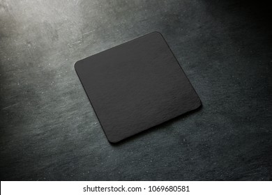 Blank black beer coaster mockup lying on grey desk. Square clear dark bar cork table-mat design mock up top side view. Quadrate cup or bottle rug display, isolated.