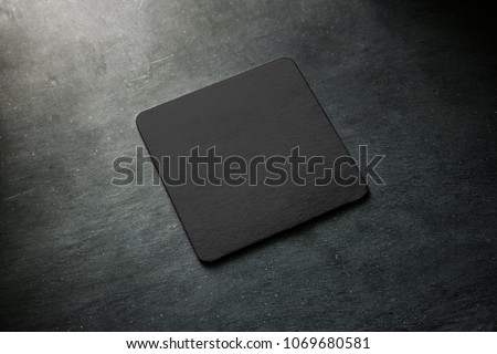 Blank black beer coaster mockup lying on grey desk. Square clear dark bar cork table-mat design mock up top side view. Quadrate cup or bottle rug display, isolated.