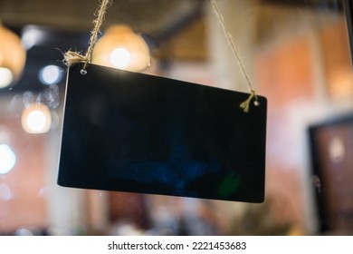 Blank Black Plastic Sign With Hang Tag On Window Door In Café Store Or Restaurant Front. Sign Hanging On Glass Board For Copyspace For Text In Sign