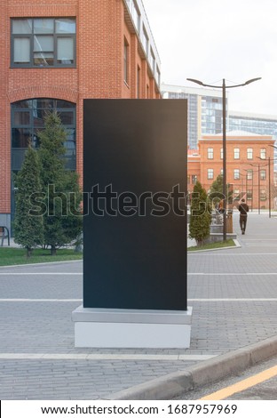 Blank black vertical pylon stand mockup brick building background. Empty rectangular street tower or monitor for promotion mock up. Clear information screen for affiche or pointer mokcup template.