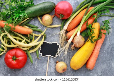 Blank blackboard label among colorful vegetables on grey stone background. Copy space.