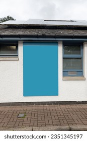 Blank blue rectangular sign on the side of a white building by a brick sidewalk