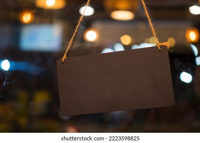 Blank Brown Plastic Sign With Hang Tag On Window Door In Café Store Or Restaurant Front. Sign Hanging On Glass Board For Copyspace For Text In Sign