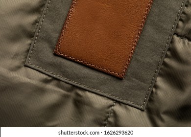 Blank Brown Round Leather Label Sewn On Puffer Jacket, Macro Close Up. Leather Patch With Stitching