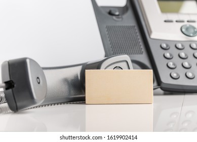 Blank business card leaning on black landline telephone in conceptual image.