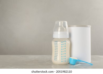 Blank Can Of Powdered Infant Formula With Feeding Bottle And Scoop On Grey Table, Space For Text. Baby Milk