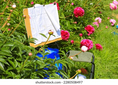 Blank canvas easel in a picturesque spring garden orchard among the blooming pink peony bushes in bloom. Artist's tools for painting a landscape in a park. Plein air painting in nature. Hobby, leisure - Powered by Shutterstock