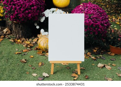 A blank canvas stands on an easel surrounded by colorful autumn flowers and pumpkins. The garden features fallen leaves, creating a beautiful seasonal backdrop. - Powered by Shutterstock