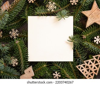 Blank Card Between Rustic Wooden Christmas Decorations And Green Fir Branches Top View. Square Card Mockup, Flat Lay, Copy Space. Christmas Or New Year Greeting Card Template, Holiday Stationery