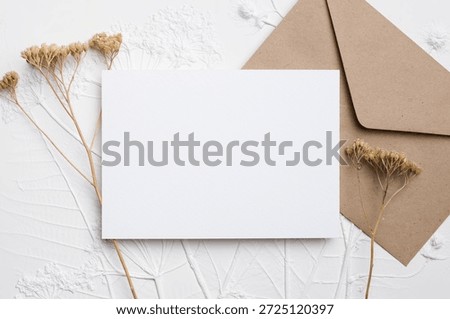 Blank card mockup featuring ample copy space, accompanied by dried flowers and a brown envelope, ideal for showcasing elegant invitations or personalized messages