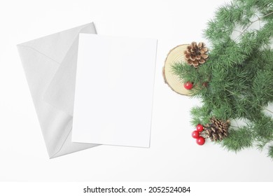 Blank card mockup with grey silver envelope with christmas decorations at the border. Pine cone, wood slice, red berry, green leaves. Holiday card, greeting card, new year card.   - Powered by Shutterstock