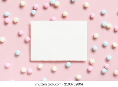 Blank card  near pastel pom-poms on light pink top view. Romantic scene with blank horizontal card with place for text  flat lay. Valentines, Spring or girlish concept
