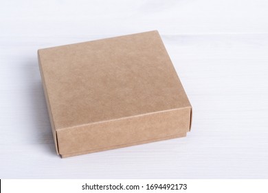 Blank Cardboard Box Package Isolated On White Wood Background. Craft Paper Box Side View. Small Square Closed Cardboard. Shipping Eco Package. Delivery Pack. Gift Idea, Eco-lifestyle. Natural Concept.