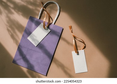 Blank cardboard brand hang tags with space for  logo, purple craft paper bag on beige background. Overlay shadows. Brand identity mock up for fashion studio.  - Shutterstock ID 2254054323