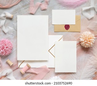 Blank cards and envelopes between pastel flowers, silk ribbons and feathers on marble top view. Romantic scene with wedding suite mockups flat lay,  place for text. Valentines, Spring