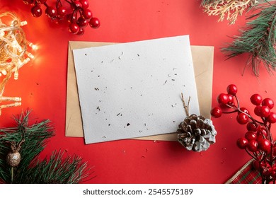 A blank Christmas card surrounded by festive decorations including a pine cone, red berries, and fairy lights on a red background, creating a warm holiday atmosphere. - Powered by Shutterstock