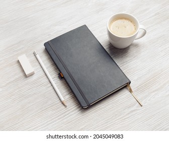 Blank closed notebook, pencil, eraser and coffee cup on light wood table background.