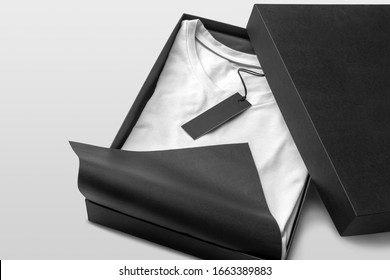 Blank Clothing Box, Package With White Blank T-shirt And Black Tag Label Mockup To Place Your Design, On A White Background. Isometric View View Fashion Branding Scene