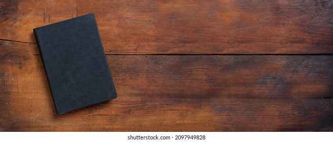 Blank Cover Book On A Table. Closed Old Black Hardcover Notebook On Wooden Background, Top View, Banner. Copy Space, Template 
