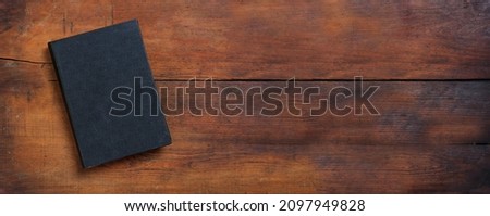 Blank cover book on a table. Closed old black hardcover notebook on wooden background, top view, banner. Copy space, template 