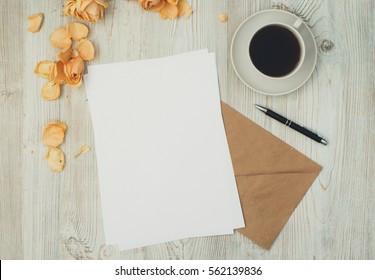 Blank Craft Envelope, Sheets Of White Paper, Pen, And Morning Coffee Cup On Wooden Desk With Rose Petals, Romantic Background For Letter Writing, Creative Work Concept