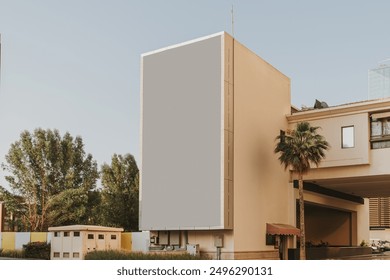 Blank digital billboard on the side of a building with palm tree and clear sky in the background - Powered by Shutterstock