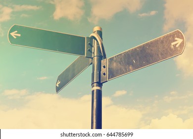 Blank directional road signs against blue sky. Black metal arrows on the signpost. Warm toned colors.  Old style image 