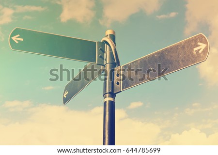 Blank directional road signs against blue sky. Black metal arrows on the signpost. Warm toned colors.  Old style image 