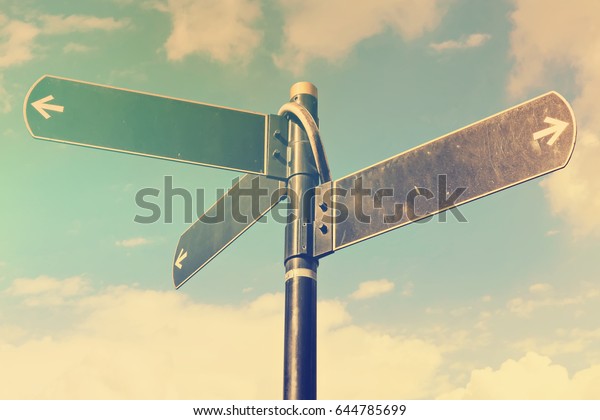 Blank\
directional road signs against blue sky. Black metal arrows on the\
signpost. Warm toned colors.  Old style image\
