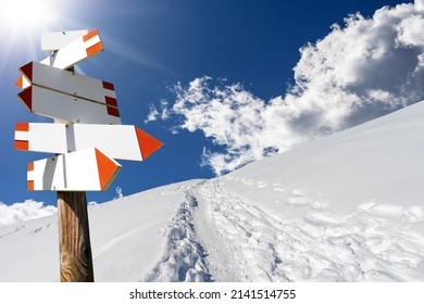 Blank directional trail signs in a beautiful winter mountain landscape with powder snow and footprints against a clear blue sky and sunbeams. Italian Alps, Italy, Europe.