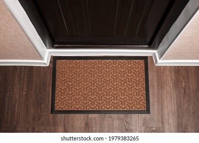 Blank Doormat Before The Dark Door In The Hall. Top View Of Mat On Wooden Floor. Mockup For Your Design