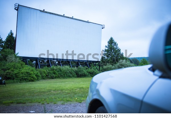 Blank drive-in movie screen; with one car waiting\
for the feature film to\
begin.
