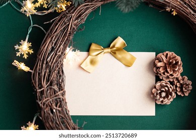 Blank empty Christmas card with a yellow gold ribbon bow on a natural wooden grapevine wreath frame for Christmas decorations with soft snowflake string lights, pine cones, green background DIY - Powered by Shutterstock