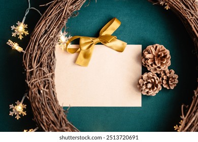 Blank empty Christmas card with a yellow gold ribbon bow on a natural wooden grapevine wreath frame for Christmas decorations with soft snowflake string lights, pine cones, green background DIY - Powered by Shutterstock