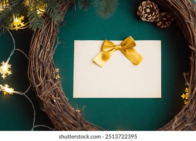 Blank empty Christmas card with a yellow gold ribbon bow on a natural wooden grapevine wreath frame for Christmas decorations with soft snowflake string lights, pine cones, green fabric background DIY - Powered by Shutterstock