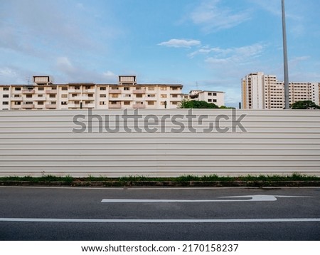 Blank empty construction hoarding in front of housing flats. Advertisement mockup in a residential neighbourhood. Fenced up construction site area.