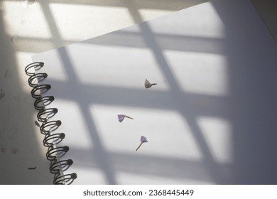 The blank empty page of the opened spiral-spine vintage square notebook is isolated on a textured white desk, under the styled sunlight , for art drawing, text, word, sketch, logo design mockup.