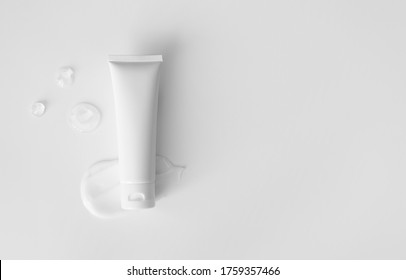 Blank empty white plastic tube for moisturizer, lotion, facial cleanser or shampoo and clear gel drops on white background with copy space, top view. Delicate purity skin care product