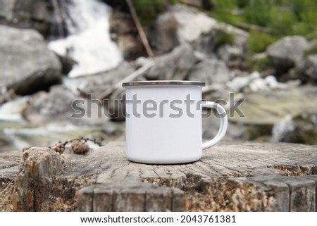 Blank enamel coffee mug, white camping cup mockup in wild nature.