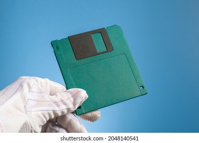 Blank Floppy Disc Of Green Color In Hand, On A Blue Background. Outdated Retro Digital Media. Old Computer Technology.