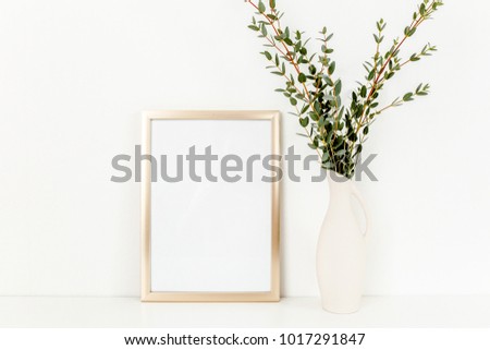 Blank frame mockup with a branches of eucalyptus in vase on table on light background. Home decor. Blog, website or social media concept.